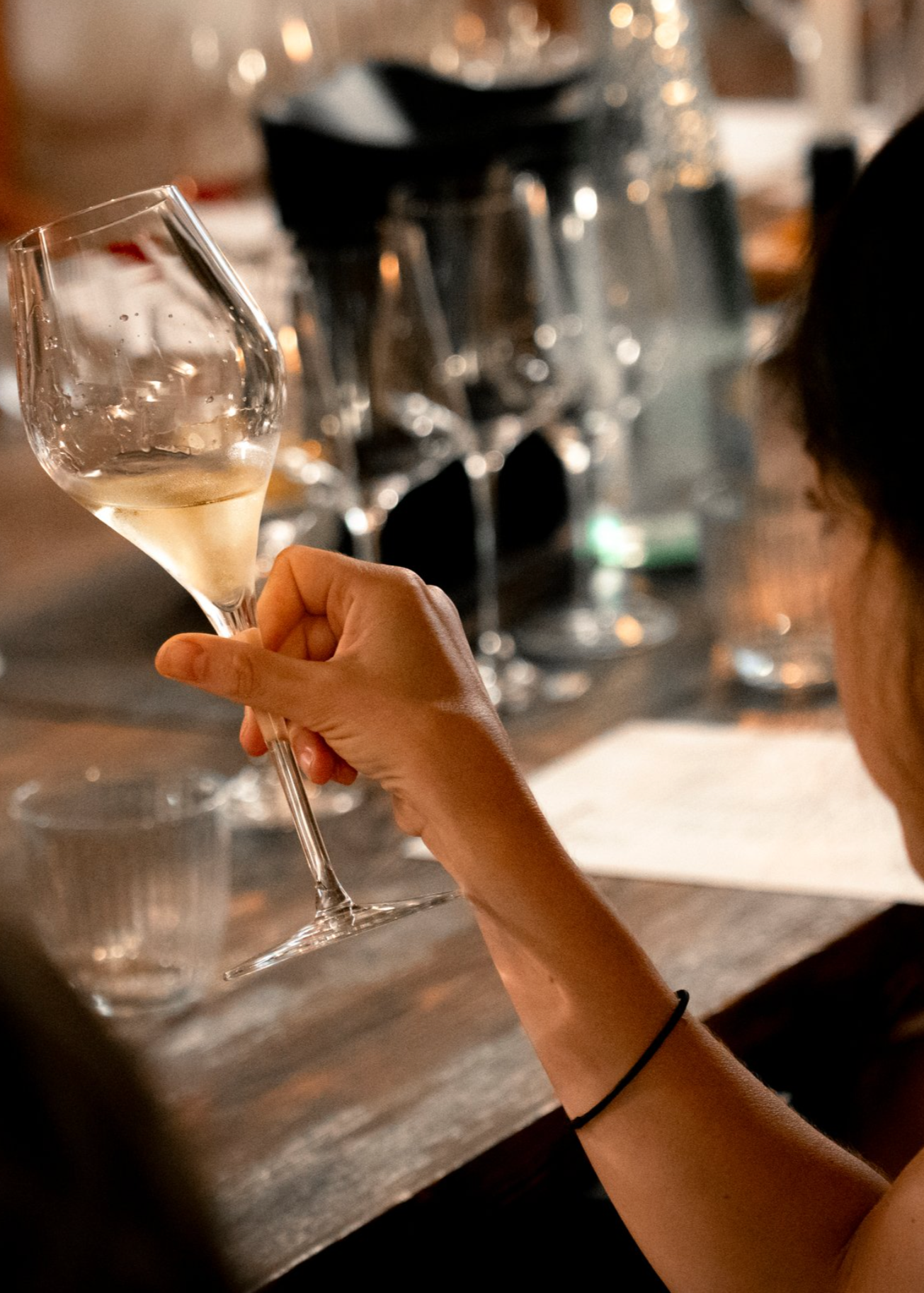 Person holding a wine glass at a table with other glasses and bottles in the background