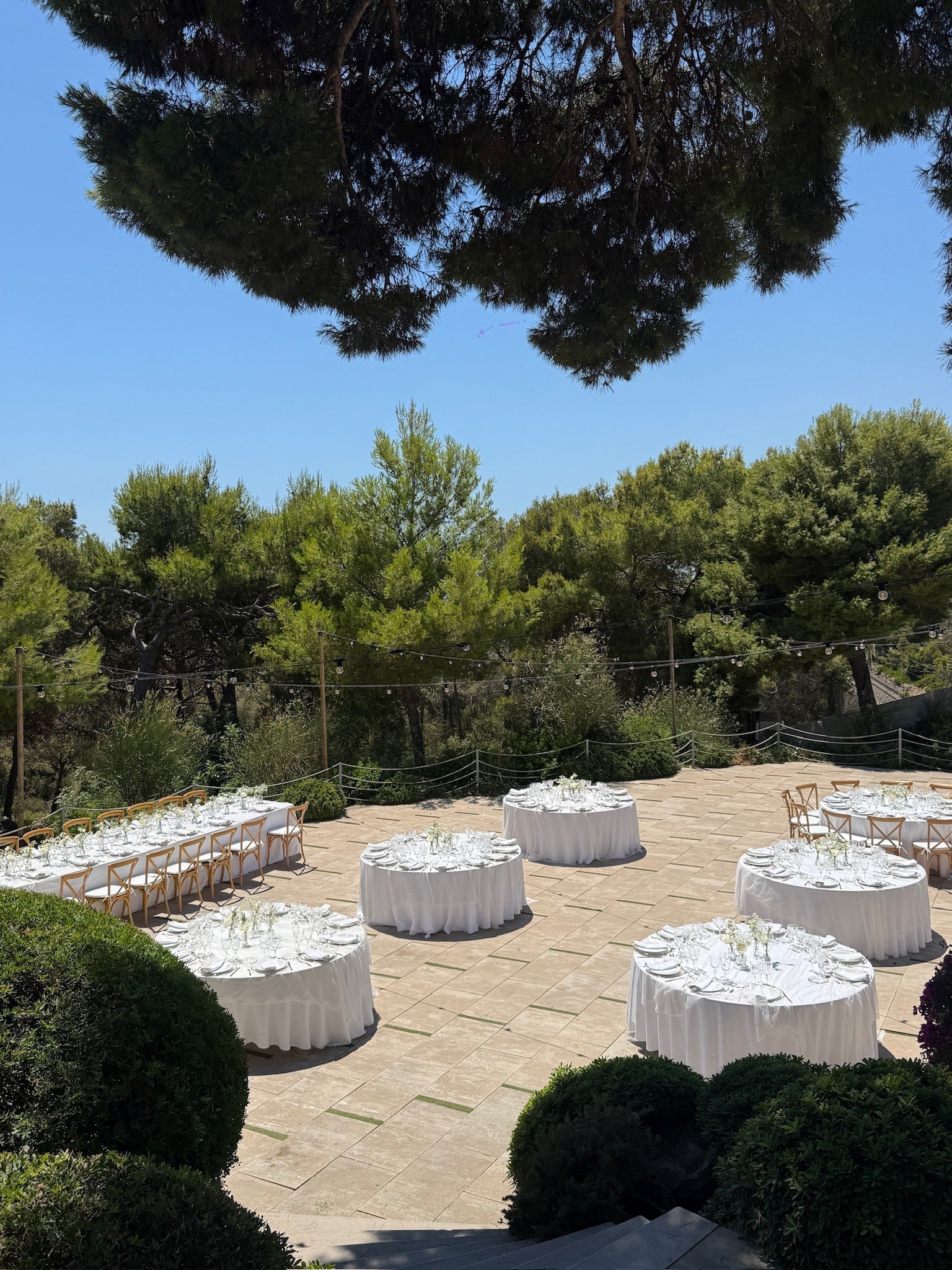 A beautifully styled outdoor wedding reception with elegant white table settings, lush greenery, and warm string lights, creating a romantic and luxurious atmosphere.