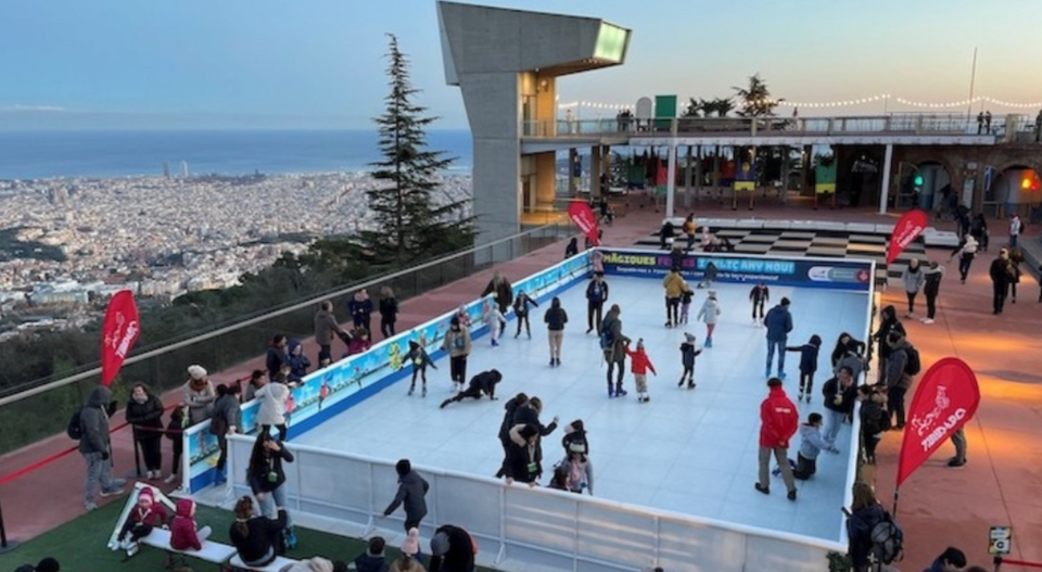 Outdoor ice skating rink in Barcelona at sunset, set on a scenic viewpoint overlooking the city and the sea, with people skating, festive lights, and a cozy winter atmosphere perfect for a romantic or playful winter date.