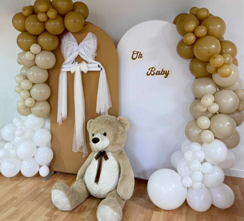 Neutral baby shower backdrop with beige and white balloon arches, “Oh Baby” signage, and a large teddy bear creating a soft, elegant celebration setup.