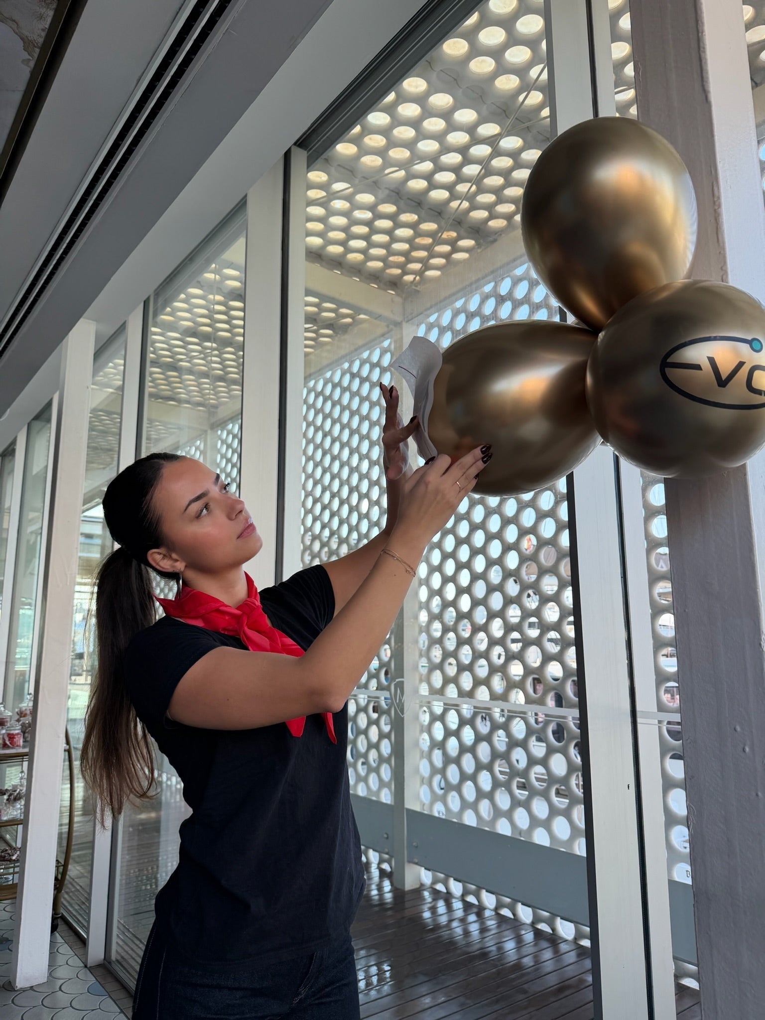 Event planner decorating a venue by attaching gold balloons with a company logo to a glass wall.