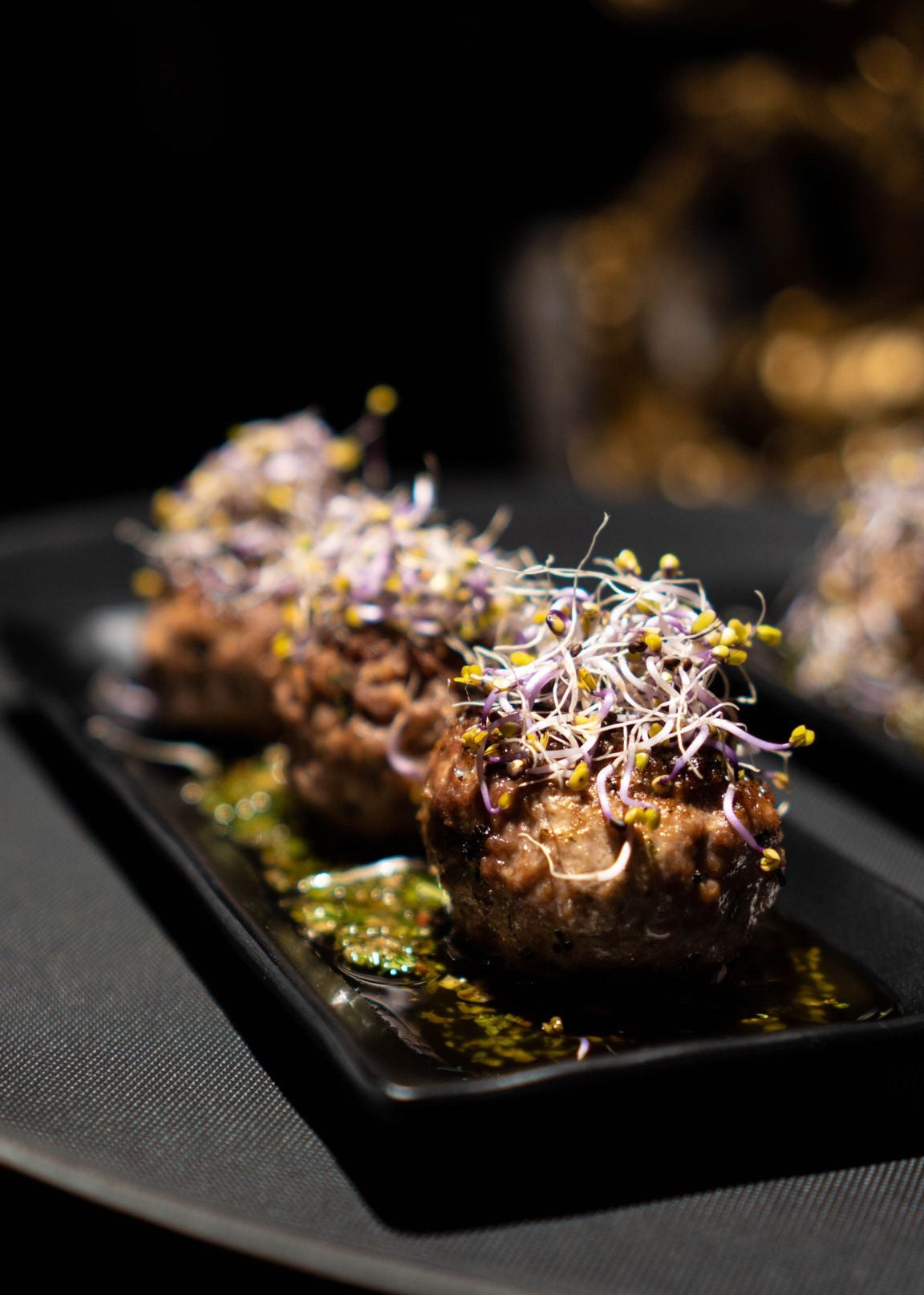 Dish of small meatballs with green sauce and herbs on a black plate from our private chef service in Barcelona. 