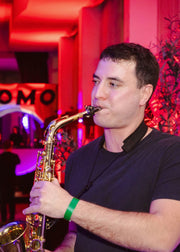 Man playing saxophone in a club with red lighting and 'OMO' sign in the background