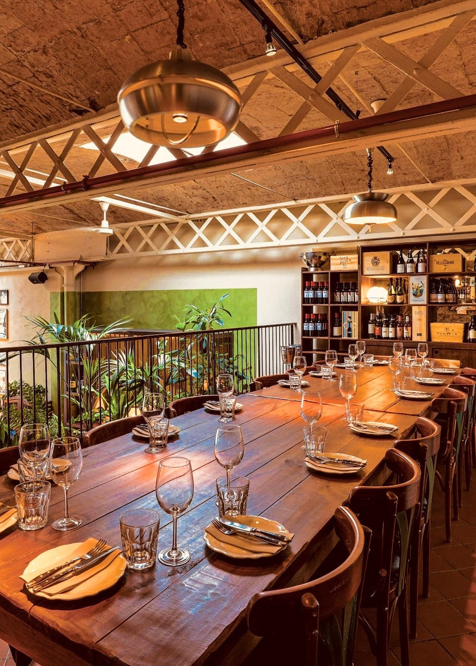Dining area with long wooden table set for a meal, surrounded by chairs, in a restaurant with wooden ceiling and balcony.