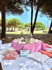 Vibrant hen party picnic in Barcelona  park near the beach, featuring a low table with colorful decorations, fresh flowers, and a view of the sea and palm trees.