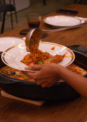 Person serving food from a pan onto a plate on a wooden table.