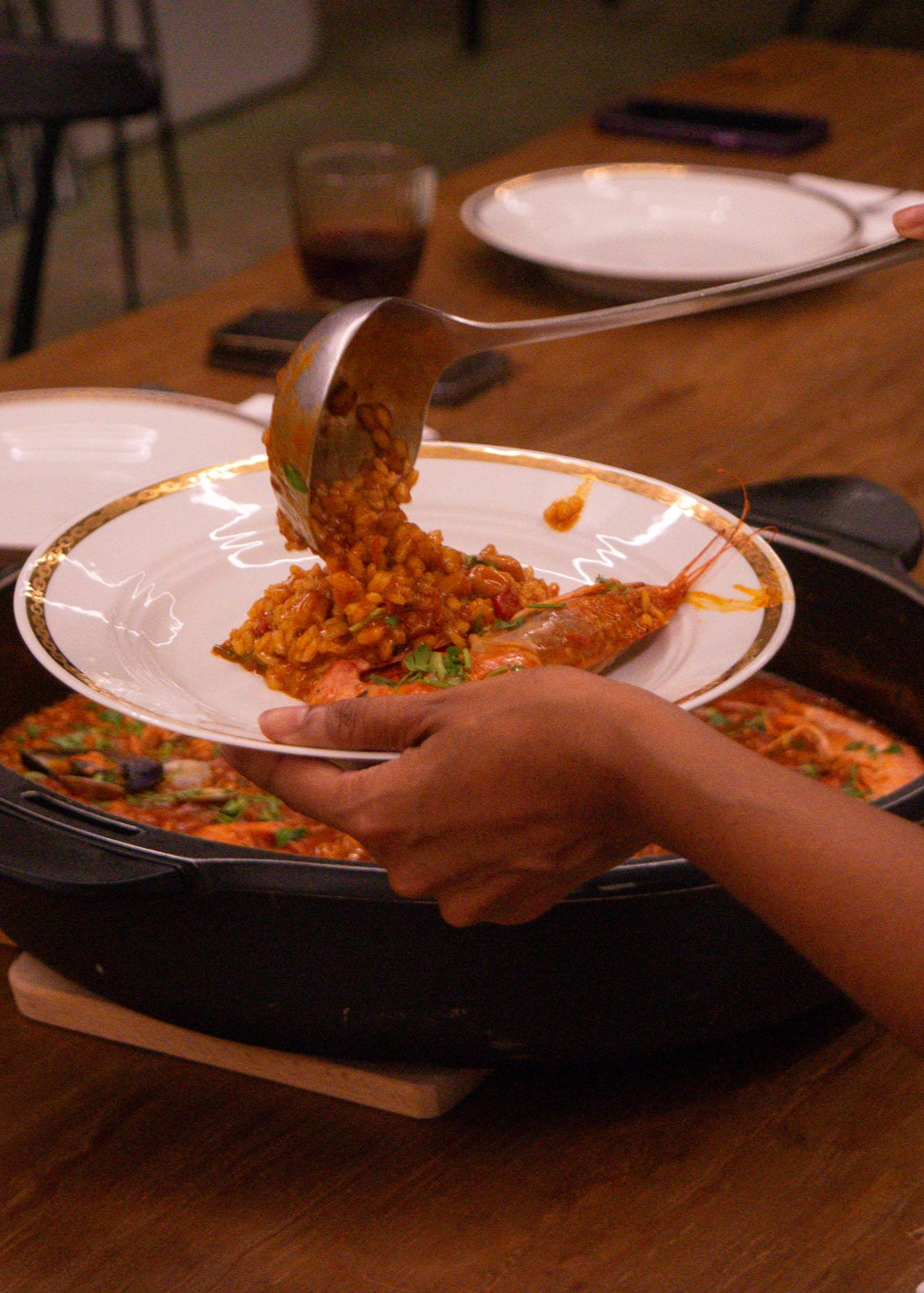 Person serving food from a pan onto a plate on a wooden table.