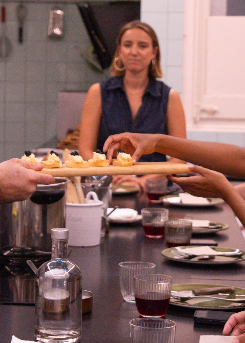 Group of people around a table with food and drinks in a kitchen setting