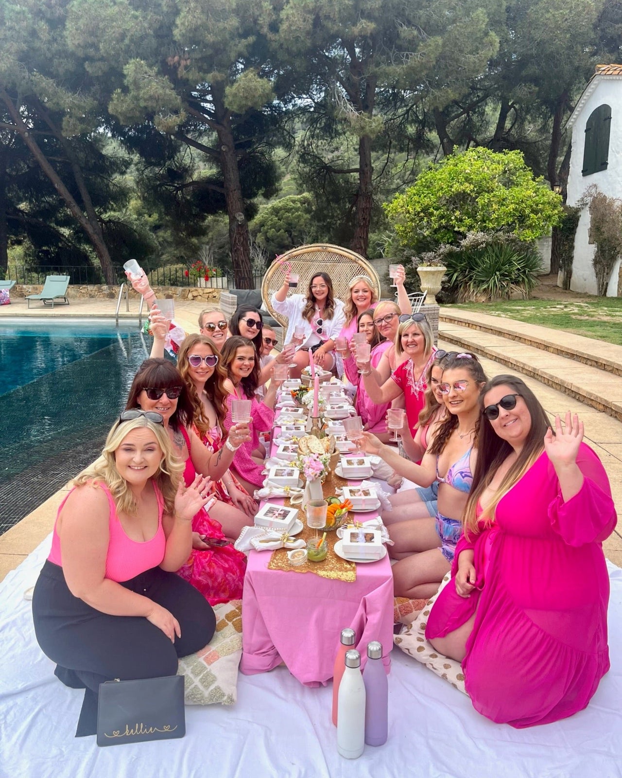 Chic hen party picnic setup at a private villa, featuring a low table with boho decor, personalized tableware, fresh flowers, and a poolside backdrop in Barcelona. 