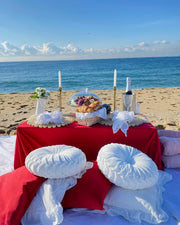 Elegant romantic picnic featuring a styled blanket, decorative pillows, a charcuterie board, fresh flowers, and candlelight, ideal for a couple's intimate outdoor celebration in Maresme.