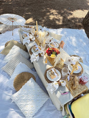 Decorated outdoor table with white tablecloth, decorative items, and a white umbrella on a sandy background.