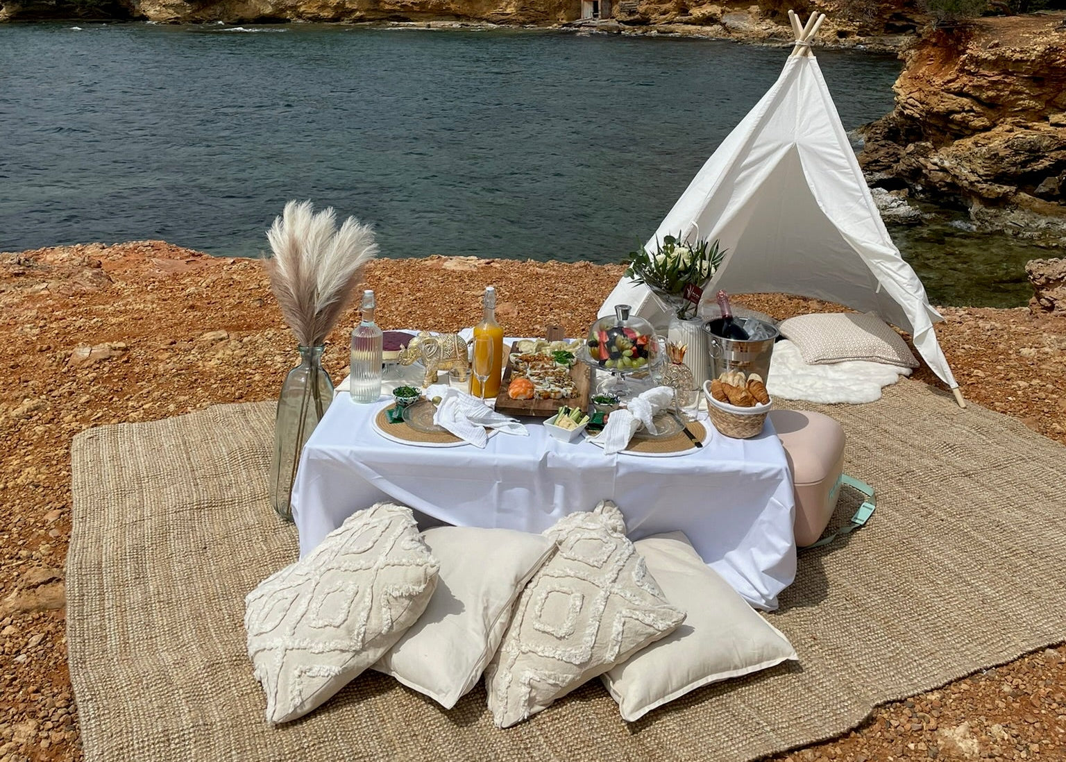 Picnic setup with a small white tent, table, and pillows by the water.