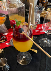 Mimosa with berries and a straw on a table with other drinks and glasses.