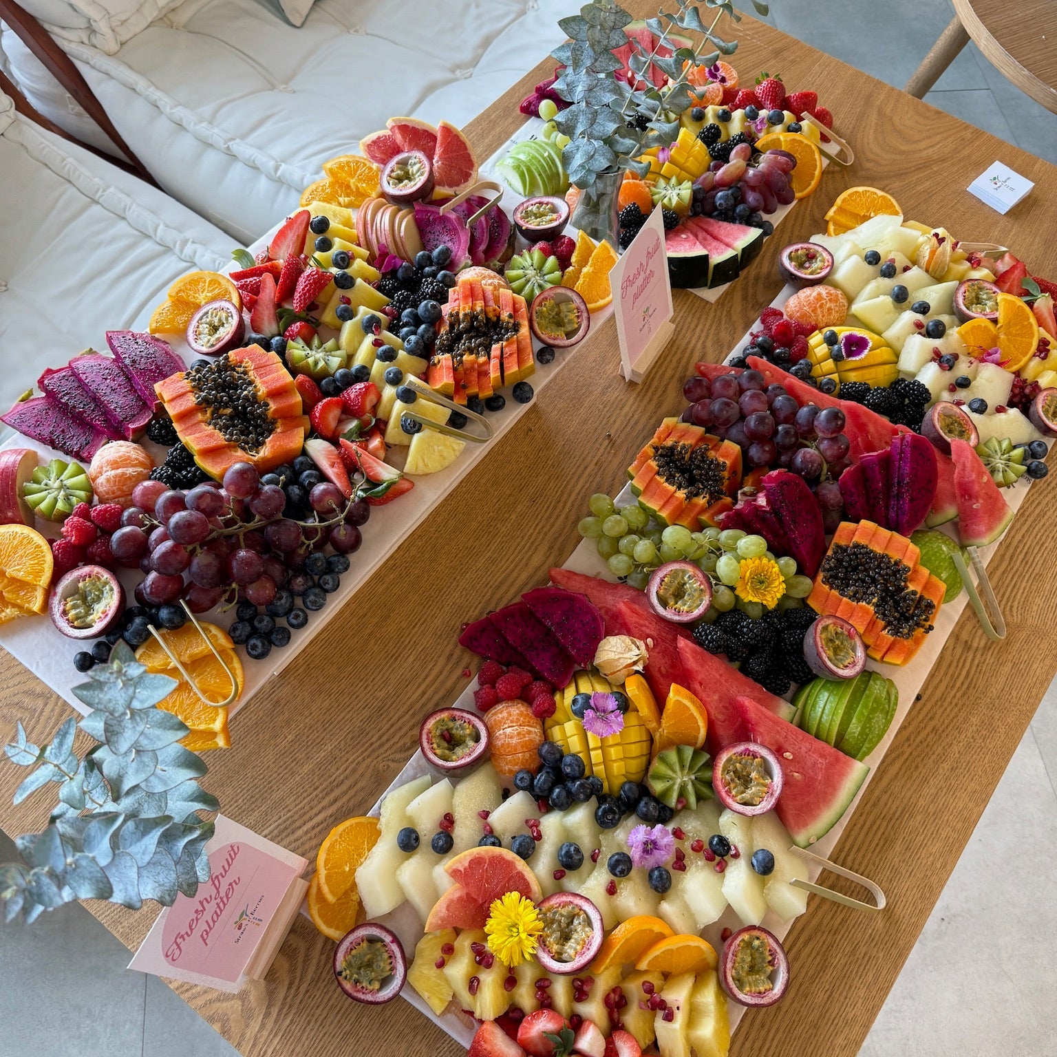 Colorful fruit platter on a wooden table with a couch and decorative pillows in the background.
