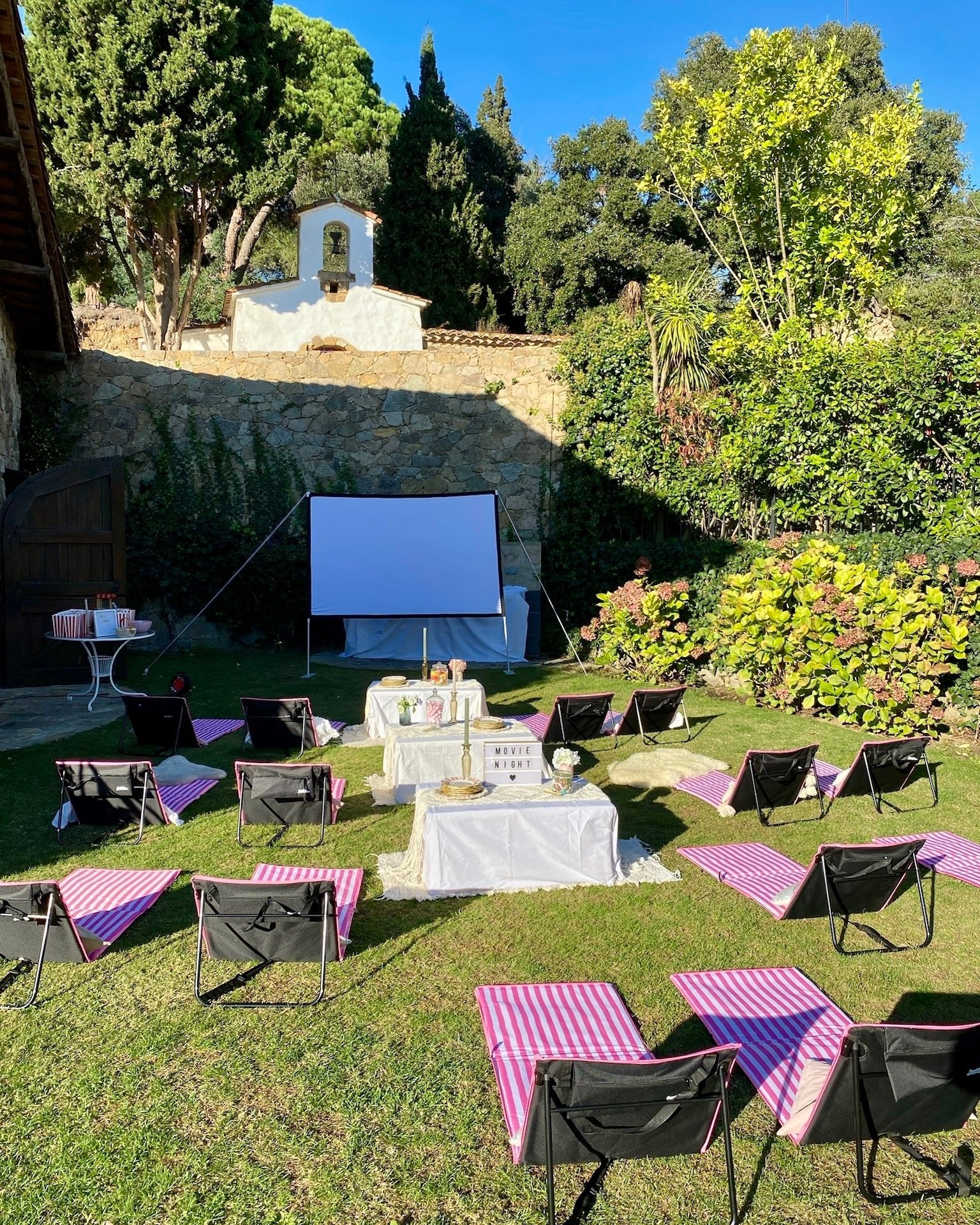 Luxury outdoor movie night and picnic at a private villa, featuring a projector screen, plush seating, ambient string lights, and a stylish grazing setup by the pool in Alella.