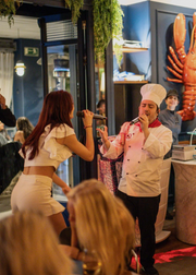 People in a restaurant with a large model of a lobster on the wall.