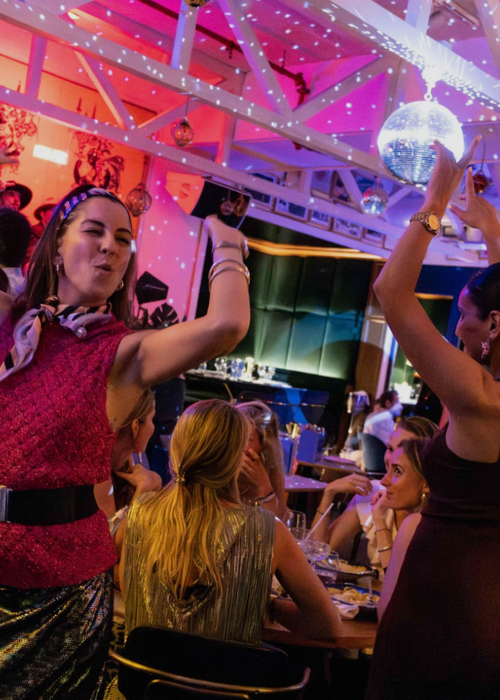 People dancing in a lively indoor setting with disco ball and colorful lights.