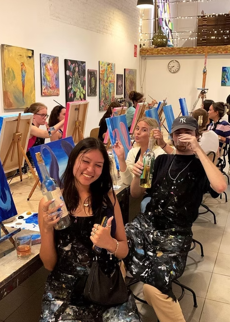 People in a studio setting with art supplies and artworks on the walls.