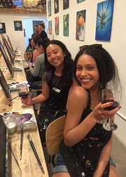 Two women sitting at a bar, holding drinks and smiling.