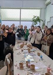 Group of people gathered around a table with craft materials, holding small framed pictures.
