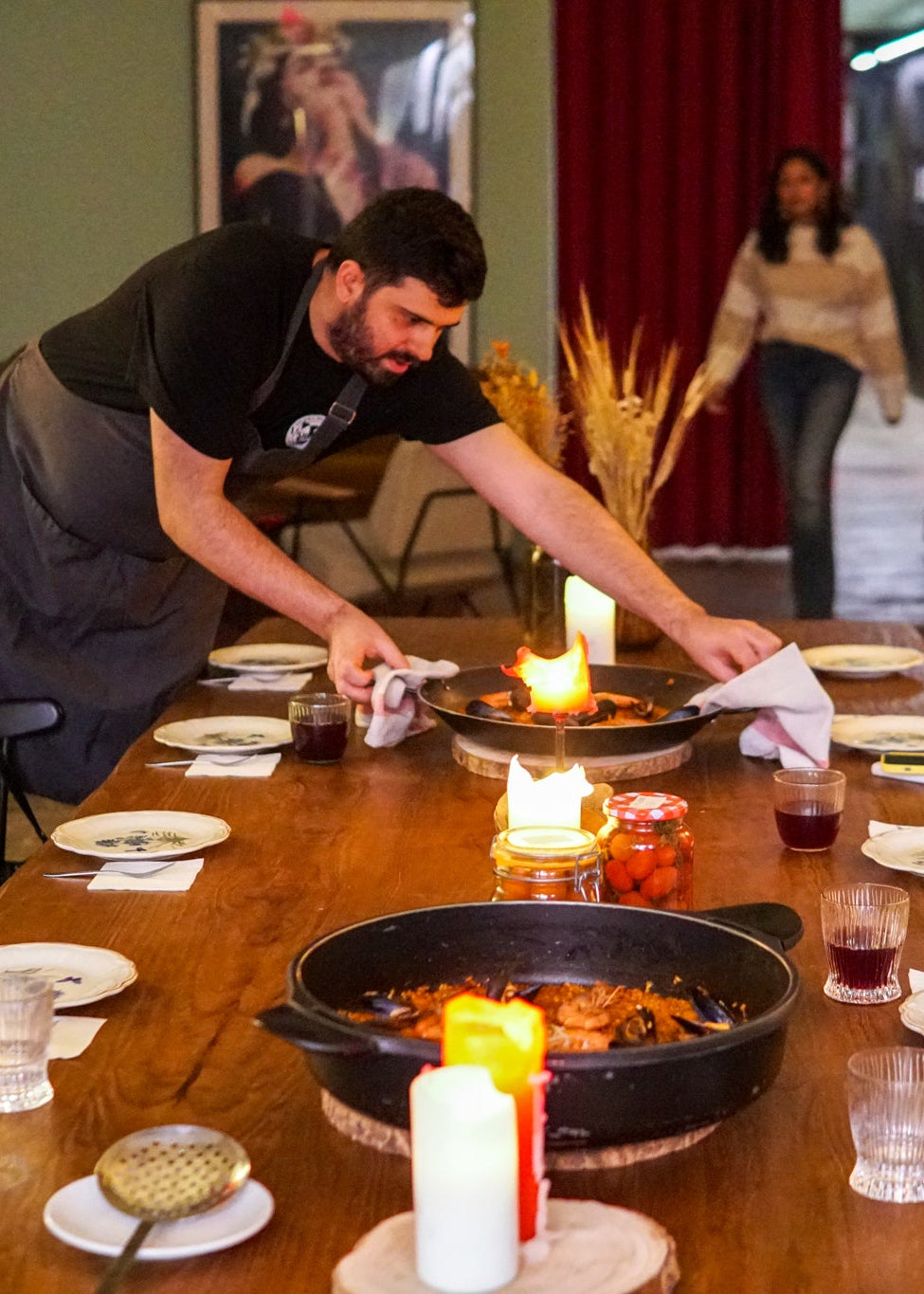 Person setting a table with candles and food in a restaurant setting