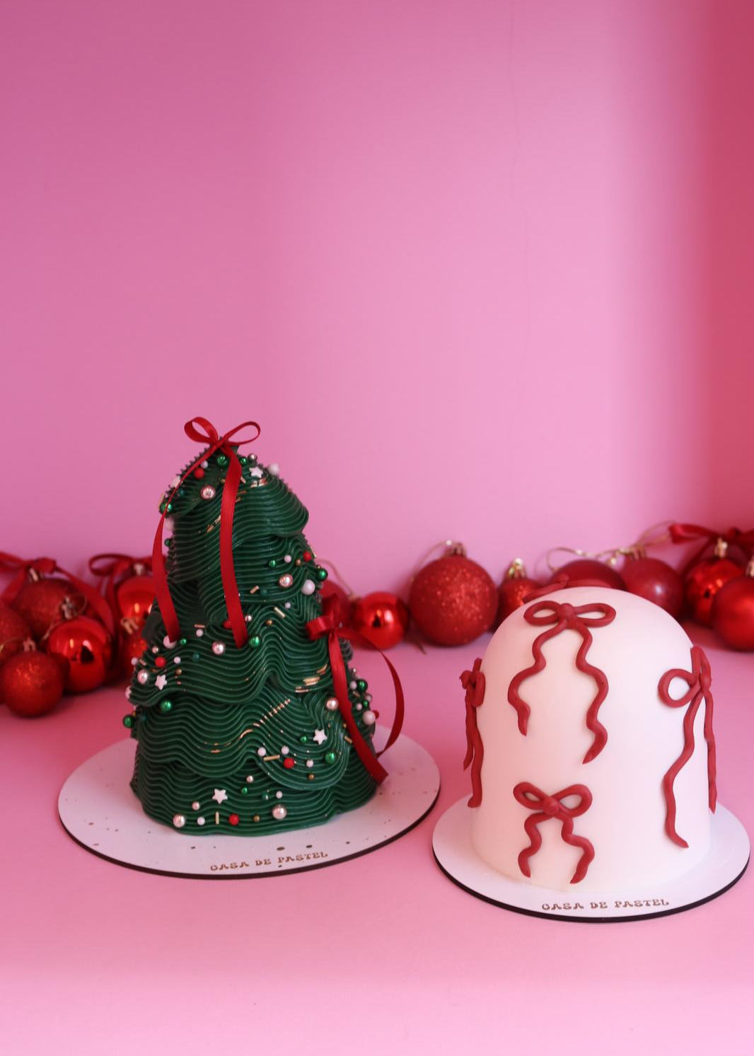 Two small cakes resembling a Christmas tree and a present against a pink background.