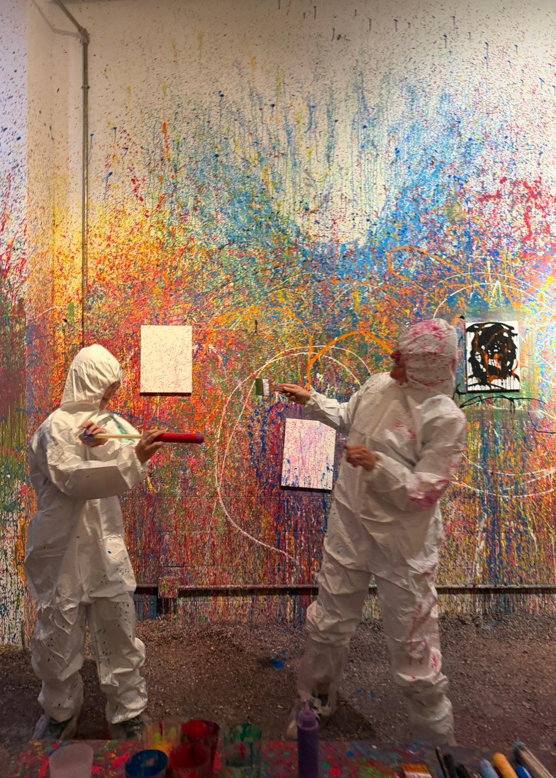 Two people in protective suits painting a colorful abstract mural on a wall.