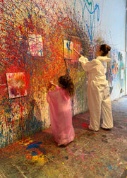Two people painting a large, colorful mural on a wall.