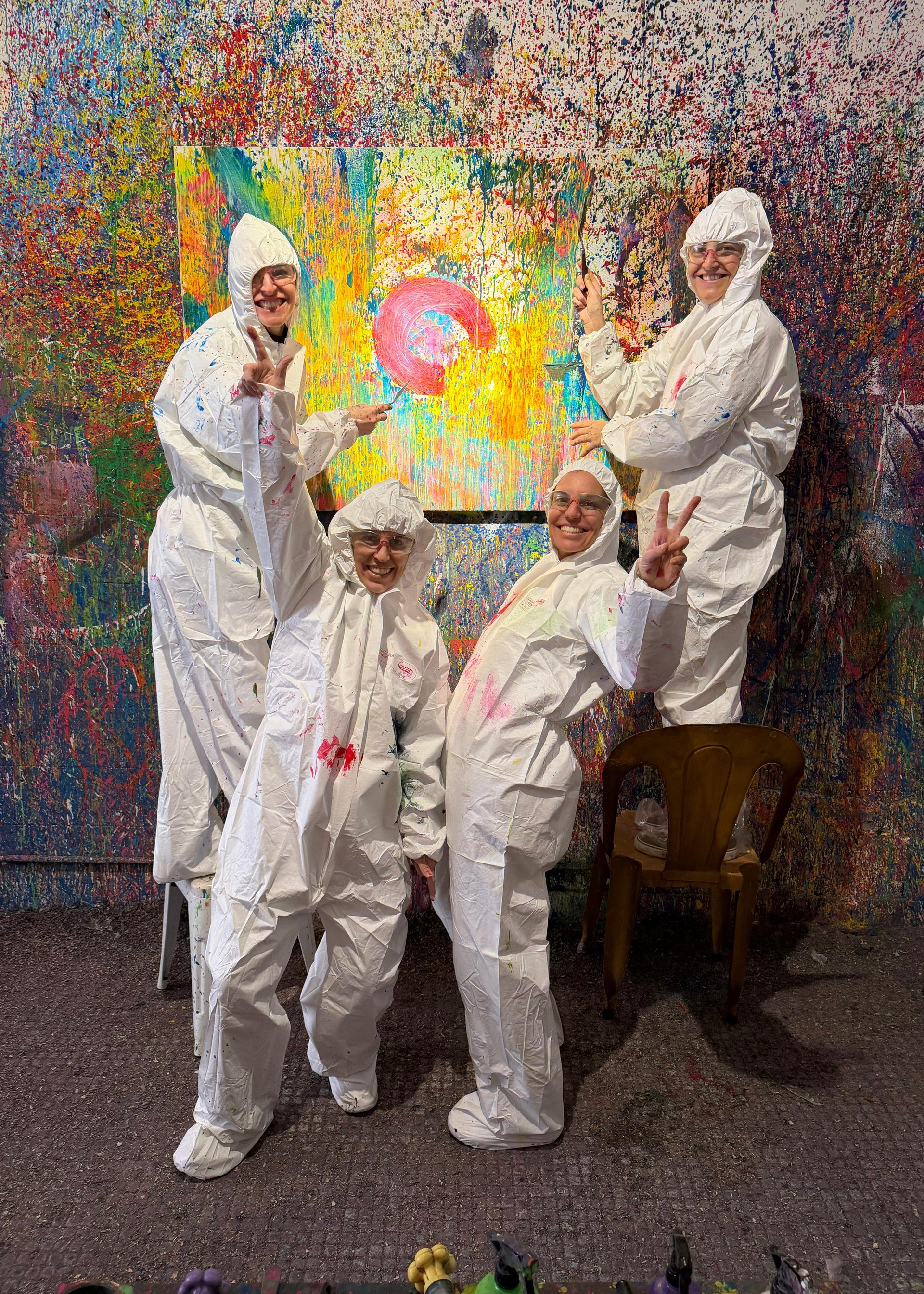 Five people in white protective suits posing in front of a colorful abstract painting.